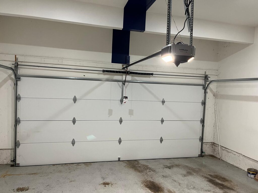 Interior view of a residential garage showing a white paneled double garage door attached to an automatic overhead opener track system in Crofton.